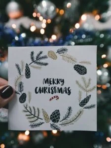 Someone holding up a Christmas Card in front of a Christmas Tree